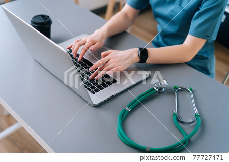 close-up of hands of unrecognizable female practitioner doctor using typing on laptop keyboard. 77727471