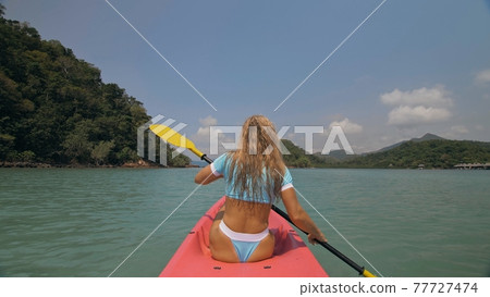 Sportive woman rows pink plastic canoe along sea water. Sportive woman rows pink plastic canoe along sea water. 77727474