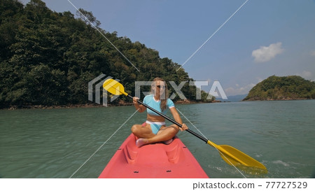 Sportive woman rows pink plastic canoe along sea water. Sportive woman rows pink plastic canoe along sea water. 77727529