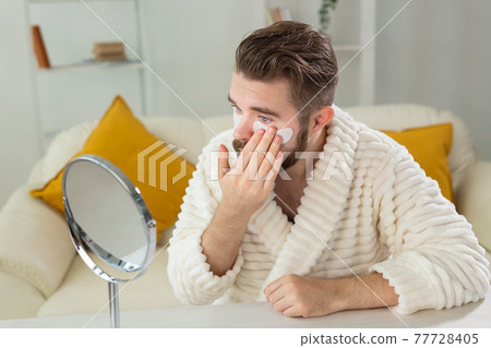 Bearded man applying eye patches on his face. Wrinkles and face home care for men. Bearded man applying eye patches on his face. Wrinkles and face home care for men. 77728405
