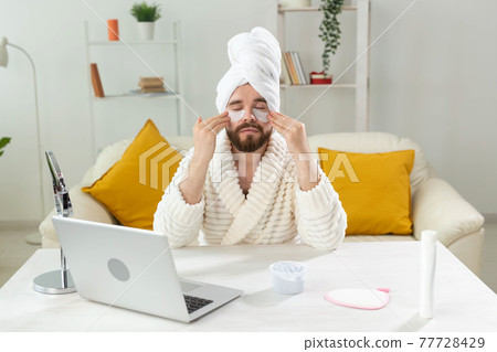 Bearded man sitting with eye patches on his face. Wrinkles and face home care for men. Bearded man sitting with eye patches on his face. Wrinkles and face home care for men. 77728429