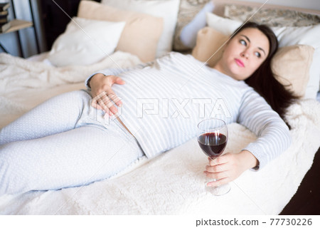 Pregnant woman keeping glass of wine. Future mother drinking alcohol while expecting little baby 77730226