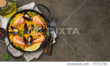 Traditional spanish seafood paella in pan with chickpeas, shrimps, mussels, squid on brown concrete background. Top view with copy space. Banner 77731783