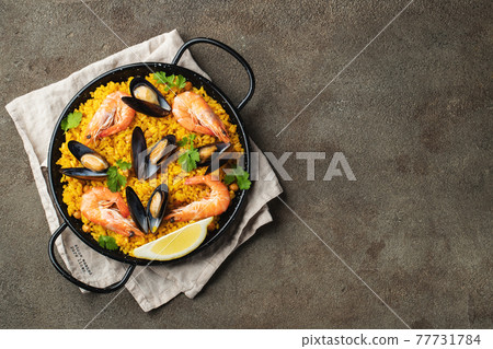 Traditional spanish seafood paella in pan with chickpeas, shrimps, mussels, squid on brown concrete background. Top view with copy space 77731784