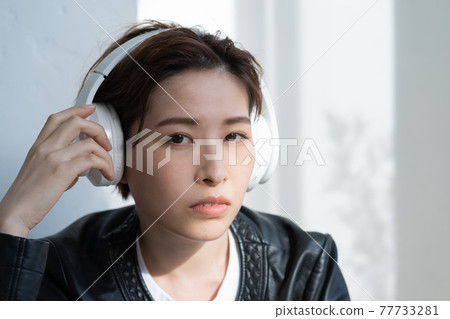A woman wearing a genderless LGBT leather jacket and listening to music with headphones 77733281