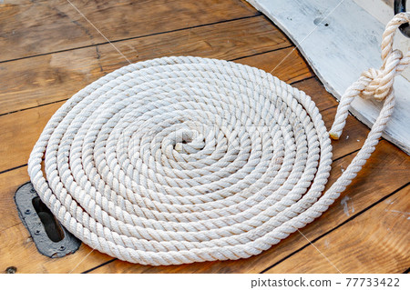 Mooring rope rolled into roll rings on a wooden board of an old boat. 77733422