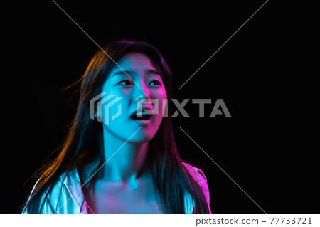 Asian young woman's portrait on dark studio background in neon. Concept of human emotions, facial expression, youth, sales, ad. 77733721