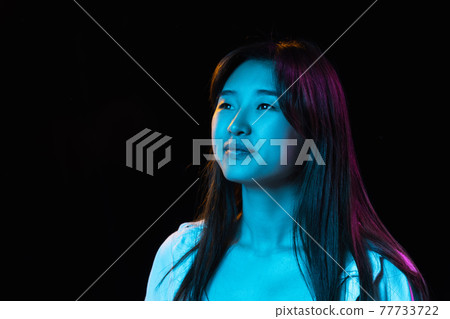 Asian young woman's portrait on dark studio background in neon. Concept of human emotions, facial expression, youth, sales, ad. 77733722