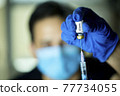 Doctor pulling vaccine liquid from vial to vaccinate man 77734055