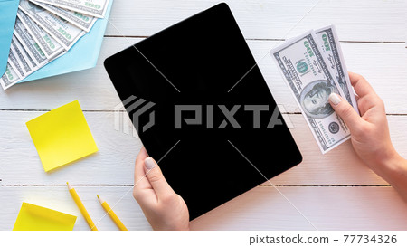 Female hands holding a tablet and money Female hands holding a tablet and money 77734326