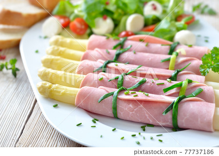 Delicious spring salad with ham asparagus rolls on a white platter, served with baguette slices Delicious spring salad with ham asparagus rolls on a white platter, served with baguette slices 77737186