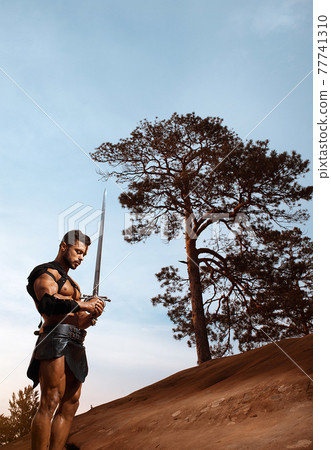 Young muscular warrior with a sword at the mountains Young muscular warrior with a sword at the mountains 77741310