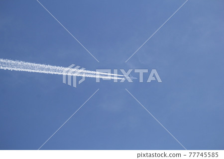 A pure white contrail that rushes straight through the blue sky, horizontal from the left 77745585