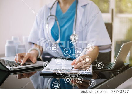 Doctor working on laptop computer and tablet and medical stethoscope on clipboard on desk, electronics medical record system EMRs concept. Doctor working on laptop computer and tablet and medical stethoscope on clipboard on desk, electronics medical record system EMRs concept. 77748277