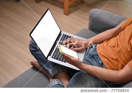 Cropped shot of man sitting on sofa and using laptop and smart phone. 77750854