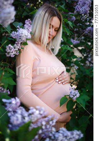 pregnant woman tenderly hugs her belly surrounded by lilac flowers 77751053