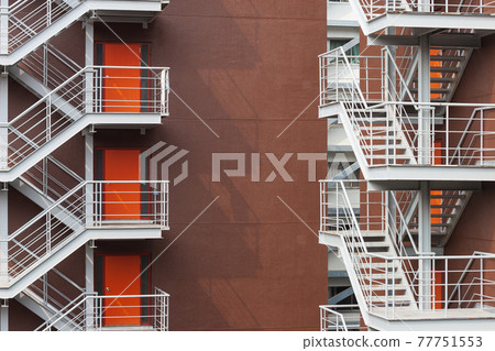 The shadow of the iron emergency stairs behind the high-rise building and the handrails falling on the wall The shadow of the iron emergency stairs behind the high-rise building and the handrails falling on the wall 77751553