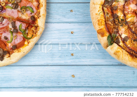 Two different delicious big pizzas on a blue wooden background Two different delicious big pizzas on a blue wooden background 77754232
