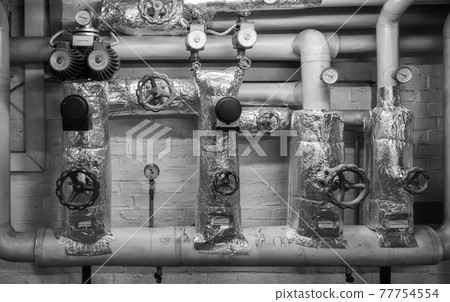 Black-and-white picture of heating pipes in the cellar with shut-off valves, thermometers, valves and throttles, jacket made of insulating wool and aluminium foil Black-and-white picture of heating pipes in the cellar with shut-off valves, thermometers, valves and throttles, jacket made of insulating wool and aluminium foil 77754554