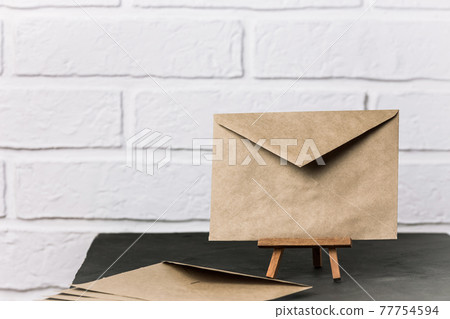 Blank envelope made of craft paper stands on a stand on a black table, communication concept in retro style, postal background with copy space Blank envelope made of craft paper stands on a stand on a black table, communication concept in retro style, postal background with copy space 77754594