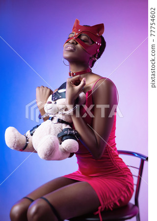 black woman in a bdsm cat mask in handcuffs with a teddy bear in her hands black woman in a bdsm cat mask in handcuffs with a teddy bear in her hands 77754602