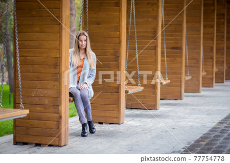 Beautiful girl in a gray knitted cardigan posing on a swing in the park 77754778