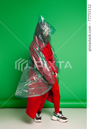 Woman in raincoat standing in studio on green background 77755532