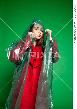 Woman in raincoat standing in studio on green background 77755569