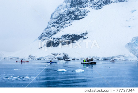 Snowfall over the motor boat with tourists and kayaks in the bay with rock and glacier in the background, near Almirante Brown, Antarctic peninsula Snowfall over the motor boat with tourists and kayaks in the bay with rock and glacier in the background, near Almirante Brown, Antarctic peninsula 77757344