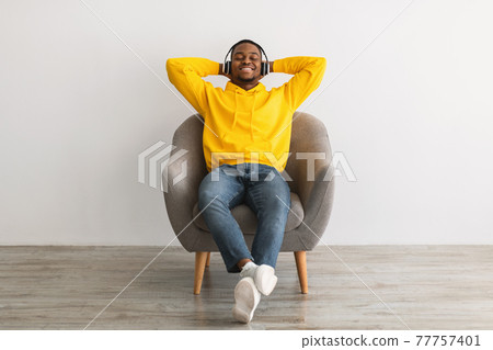 Black Guy Sitting Listening To Music In Headphones, Gray Background Black Guy Sitting Listening To Music In Headphones, Gray Background 77757401
