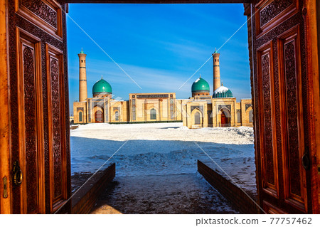 Winter shot of blue domes, mosques and minarets of Hazrati Imam medrese with wooden ornated doors in the foreground, religious center of Tashkent, Uzbekistan 77757462