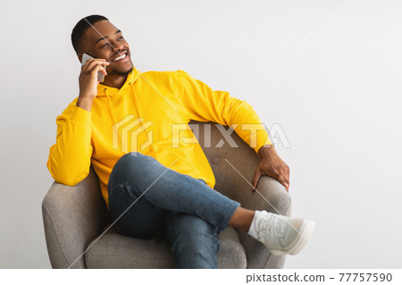 Cheerful Black Guy Talking On Phone Sitting Over Gray Background Cheerful Black Guy Talking On Phone Sitting Over Gray Background 77757590