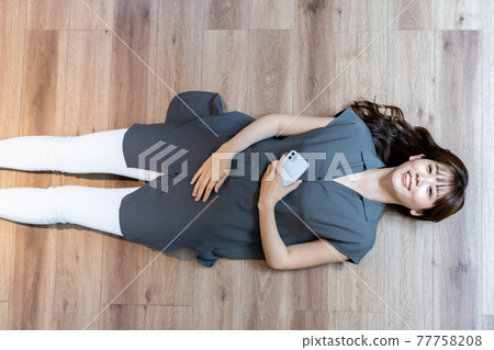A woman lying on the floor while holding a smartphone 77758208