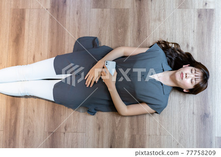 A woman lying on the floor while holding a smartphone 77758209