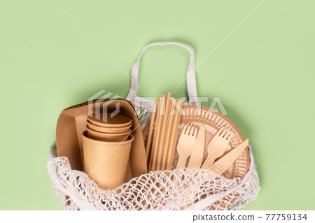 Flat lay, eco-friendly tableware - kraft paper food cups and containers with wooden cutlery in white cotton net bag on light green background with copy space. Street food take away paper packaging 77759134