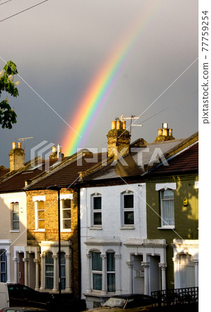 Rainbow emerges with sunlight behind terraced houses after rain Rainbow emerges with sunlight behind terraced houses after rain 77759254