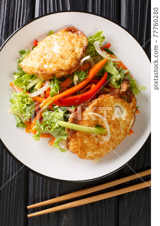 Yam khai dao fried egg spicy salad with vegetables and herbs is a Thai dish close up in the plate. Vertical top view 77760280