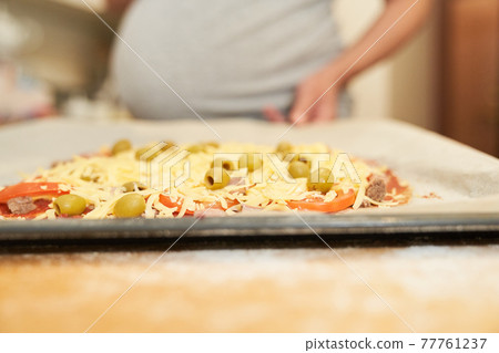 Pregnant woman holds on a baking sheet prepared for baking pizza.Cooking at home Pregnant woman holds on a baking sheet prepared for baking pizza.Cooking at home 77761237