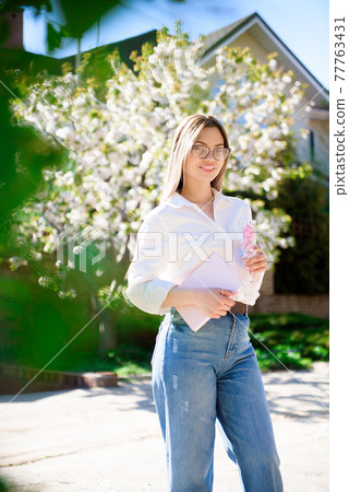 A woman in a white shirt and jeans with glasses in her hands in a spring garden. A woman in a white shirt and jeans with glasses in her hands in a spring garden. 77763431