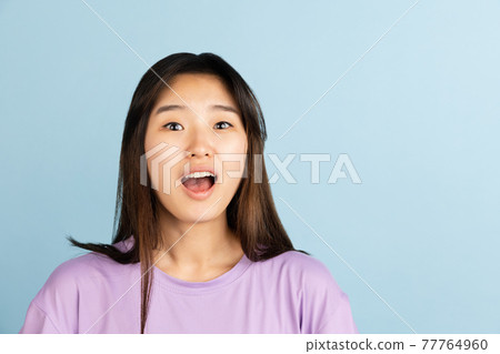 Asian young woman's portrait on blue studio background. Concept of human emotions, facial expression, youth, sales, ad. 77764960