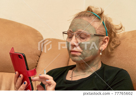 Grandmother with a cosmetic mask on her face made of healing clay Grandmother with a cosmetic mask on her face made of healing clay 77765602