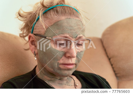 Grandmother with a cosmetic mask on her face made of healing clay Grandmother with a cosmetic mask on her face made of healing clay 77765603