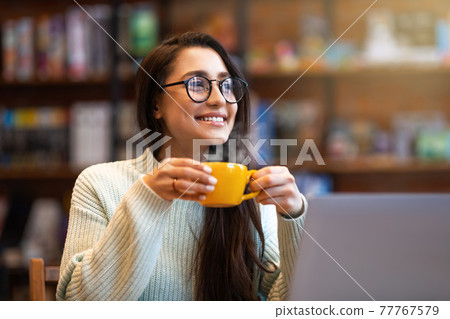 Dreamy positive latin woman relaxing at cafe, enjoying coffee or tea alone, holding mug with hot beverage Dreamy positive latin woman relaxing at cafe, enjoying coffee or tea alone, holding mug with hot beverage 77767579