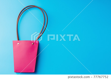 Paper shopping bag with round handles on a blue background. Flatlay with space to copy. Fashionable 77767752