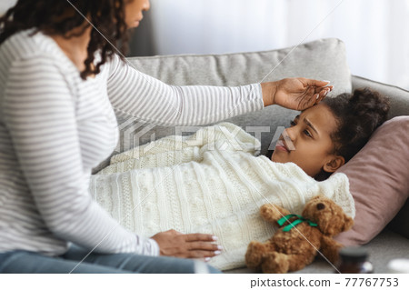 Worried mother checking her sick daughter body temperature 77767753