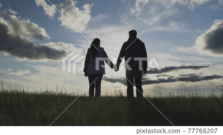Man and woman stand at sunset holding hands, teamwork, farm field Man and woman stand at sunset holding hands, teamwork, farm field 77768207