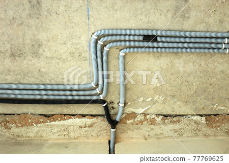 Electrical cables laid in protective corrugation installed on the ceiling and wall in a room under construction works. 77769625