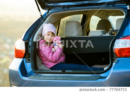 Pretty happy child girl playing with a pink toy teddy bear in a car trunk. Pretty happy child girl playing with a pink toy teddy bear in a car trunk. 77769755