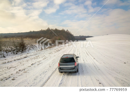 Family car driving on a dirt road in snow covered winter field. 77769959