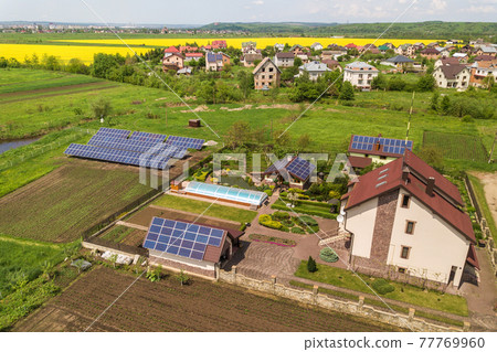 Aerial view of a private house in summer with blue solar photo voltaic panels on roof top and in the yard. Aerial view of a private house in summer with blue solar photo voltaic panels on roof top and in the yard. 77769960